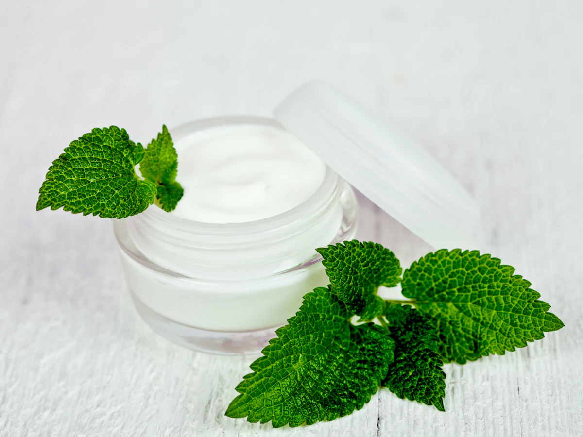 A jar of soothing cream beside fresh green leaves