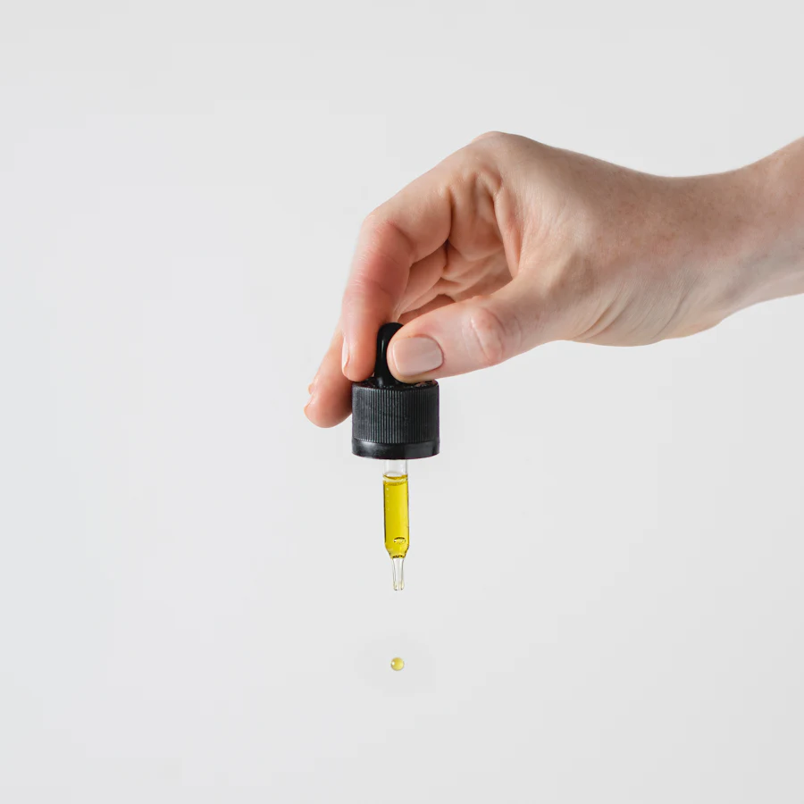 A drop of golden oil falling from a dropper