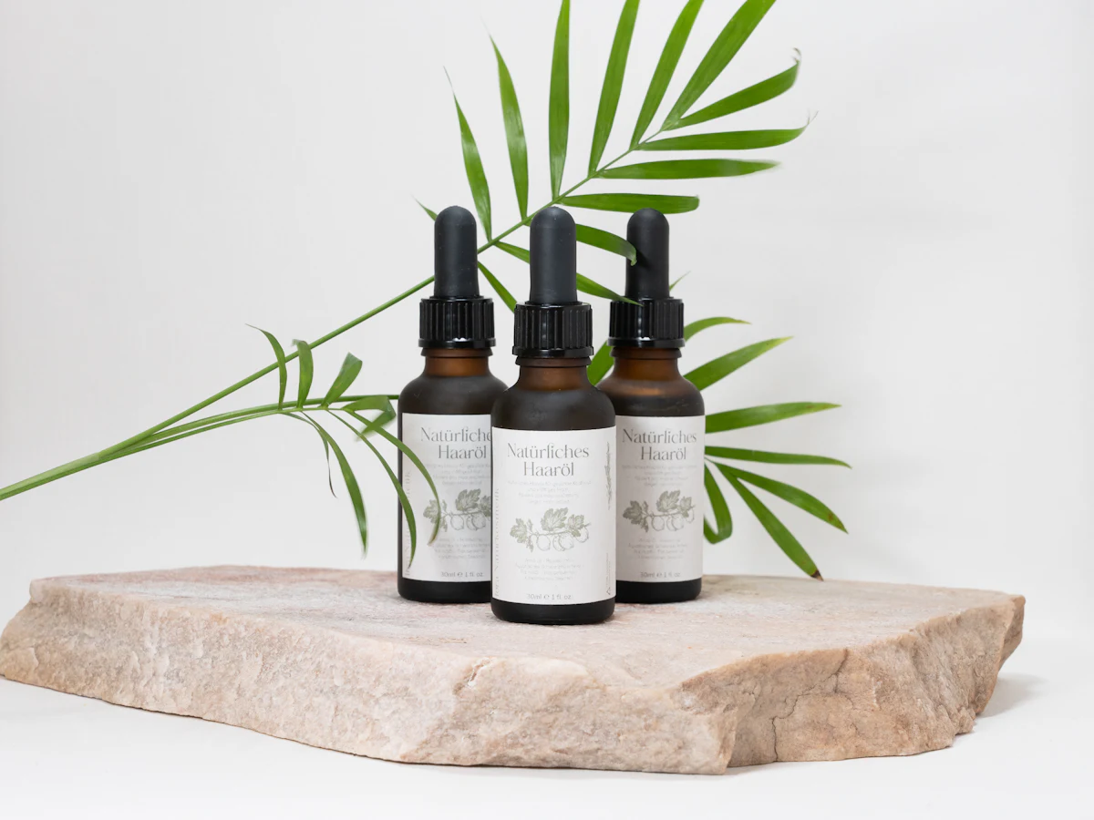 Dropper bottles of hair oil beside a palm leaf